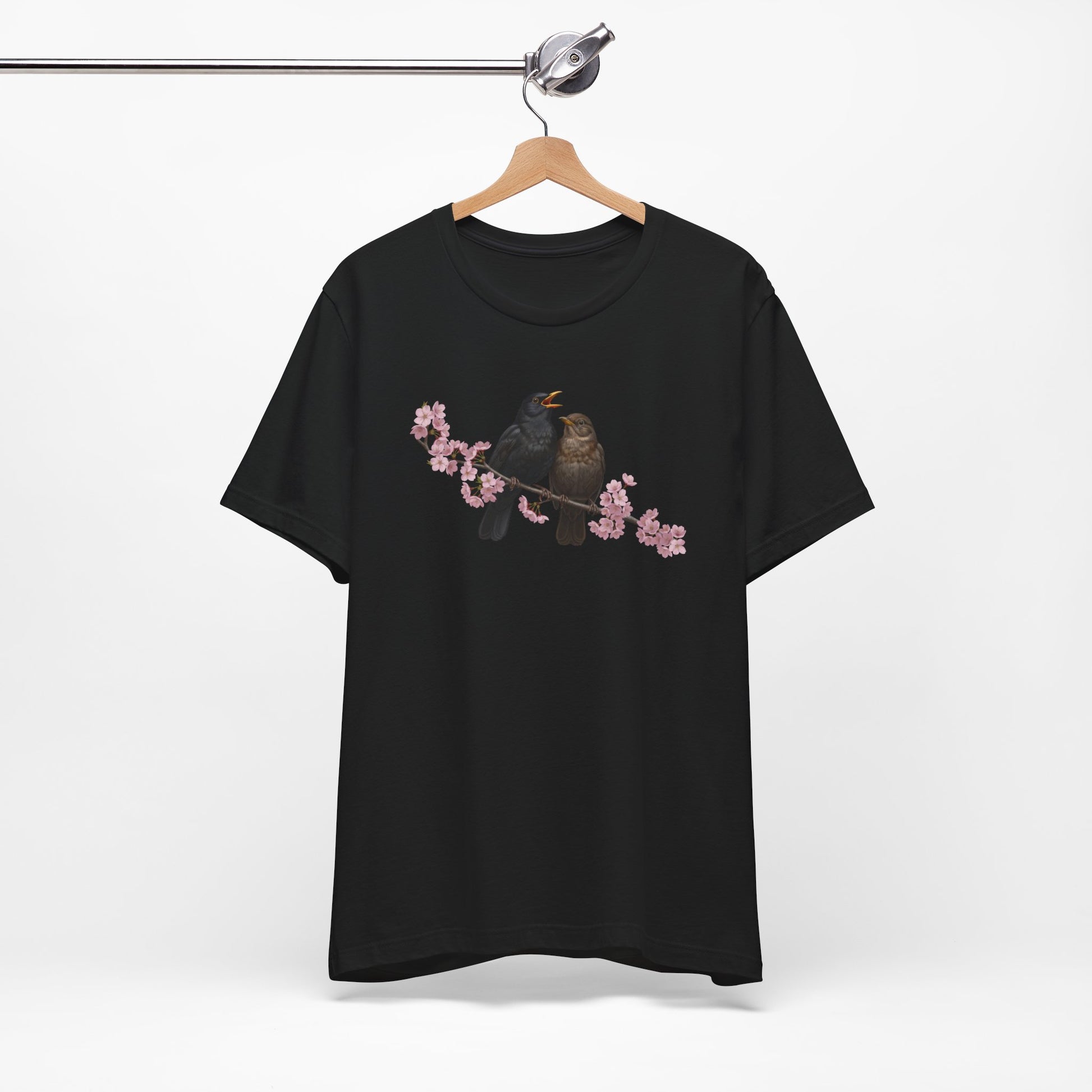 Black t-shirt with a bird and cherry blossom design on a hanger against a white background