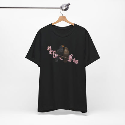 Black t-shirt with a bird and cherry blossom design on a hanger against a white background