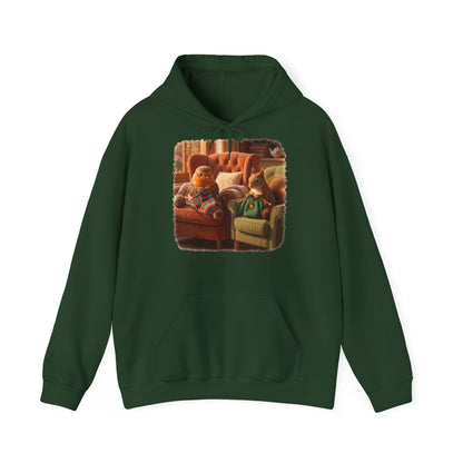 Ein dunkelgrüner Kapuzenpullover mit einem quadratischen Grafikdruck auf der Brust, der eine gemütliche Wohnzimmerszene zeigt: Ein Rotkehlchen sitzt neben einem Eichhörnchen im grünen Pullover auf einem Sessel, und beide stricken.