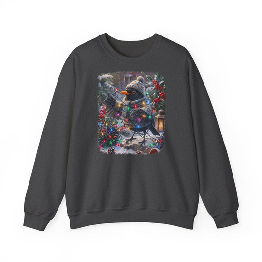 Ein dunkelgraues Sweatshirt mit Rundhalsausschnitt und einem farbenfrohen Grafikdruck: eine Amsel in Winterkleidung und mit Mütze, die inmitten von Weihnachtsbäumen und Schnee eine Lichterkette hält.