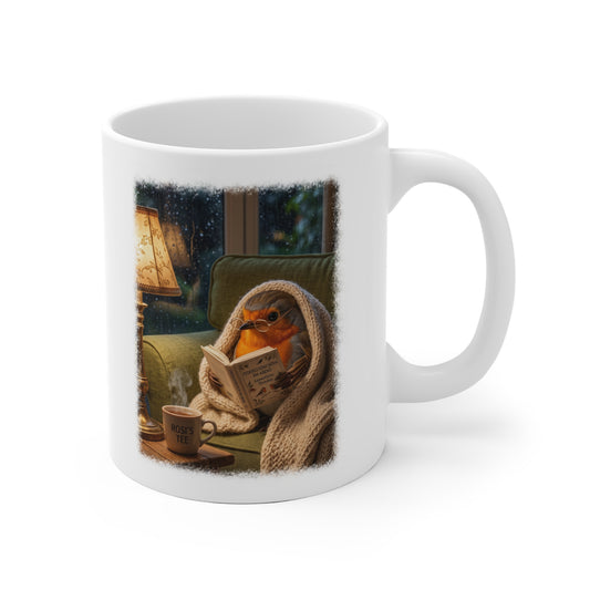 Digital gemalte Illustration eines niedlichen Rotkehlchens, das eingekuschelt auf dem Sofa ein Buch liest, gedruckt mit weichen, künstlerischen Acryl-Kanten auf einer weißen Keramiktasse.