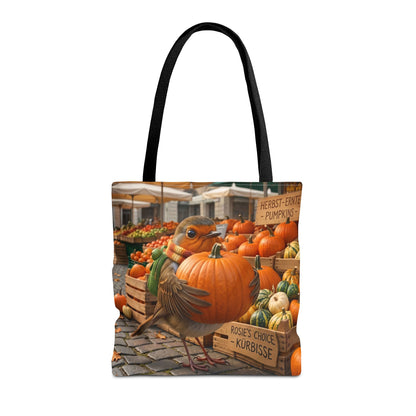 Herbstliche Tragetasche aus Stoff. Das detailreiche Motiv zeigt das kleine Rotkehlchen Rosi, das glücklich einen riesigen orangenen Kürbis auf dem Marktplatz im Arm hält. Ein praktischer und umweltfreundlicher Begleiter für den Herbsteinkauf und ein schönes Geschenk für Vogelfreunde.