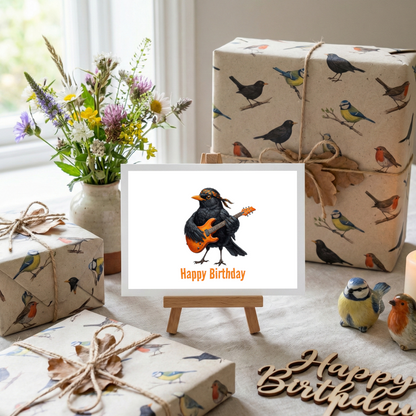 Grußkarte mit einer Amsel, die Gitarre spielt, und dem Text „Happy Birthday“ auf einem Geburtstagstisch